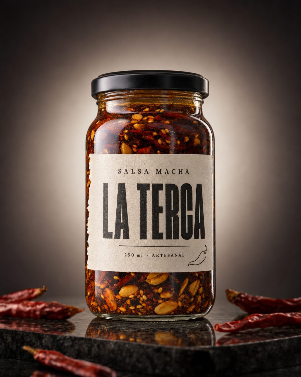 Frasco de vidrio de salsa macha sobre una piedra oscura, con luz cálida detrás y chiles secos alrededor