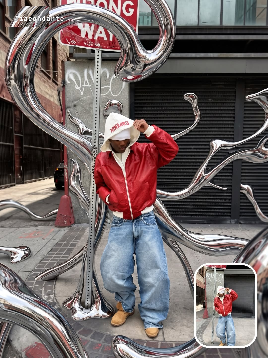 Persona con chamarra roja recargada en un poste de señal de tránsito, envuelta en tubos de cromo líquido que reflejan la calle